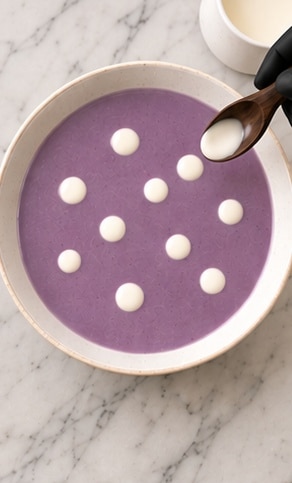 Purple cauliflower soup with cream dots and herb garnish