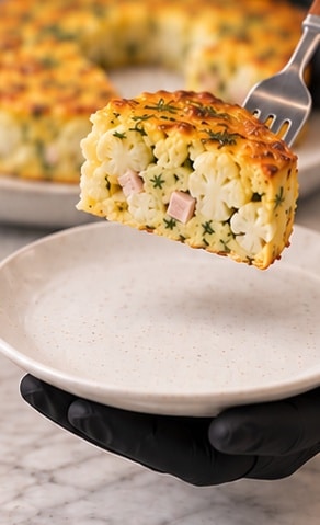 Cauliflower egg bake wedge lifted above a white ceramic serving plate
